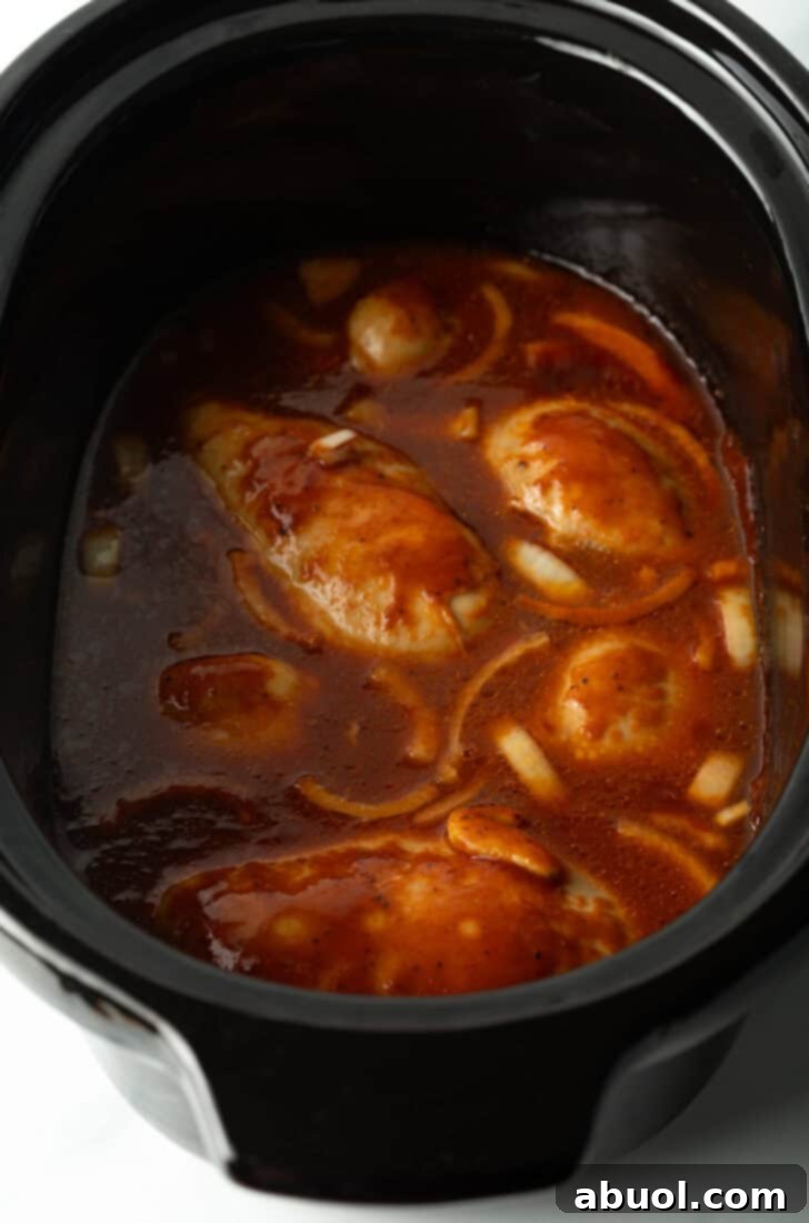 Another perspective of the crockpot filled with chicken and barbecue sauce, illustrating the thorough coating and immersion of the chicken.