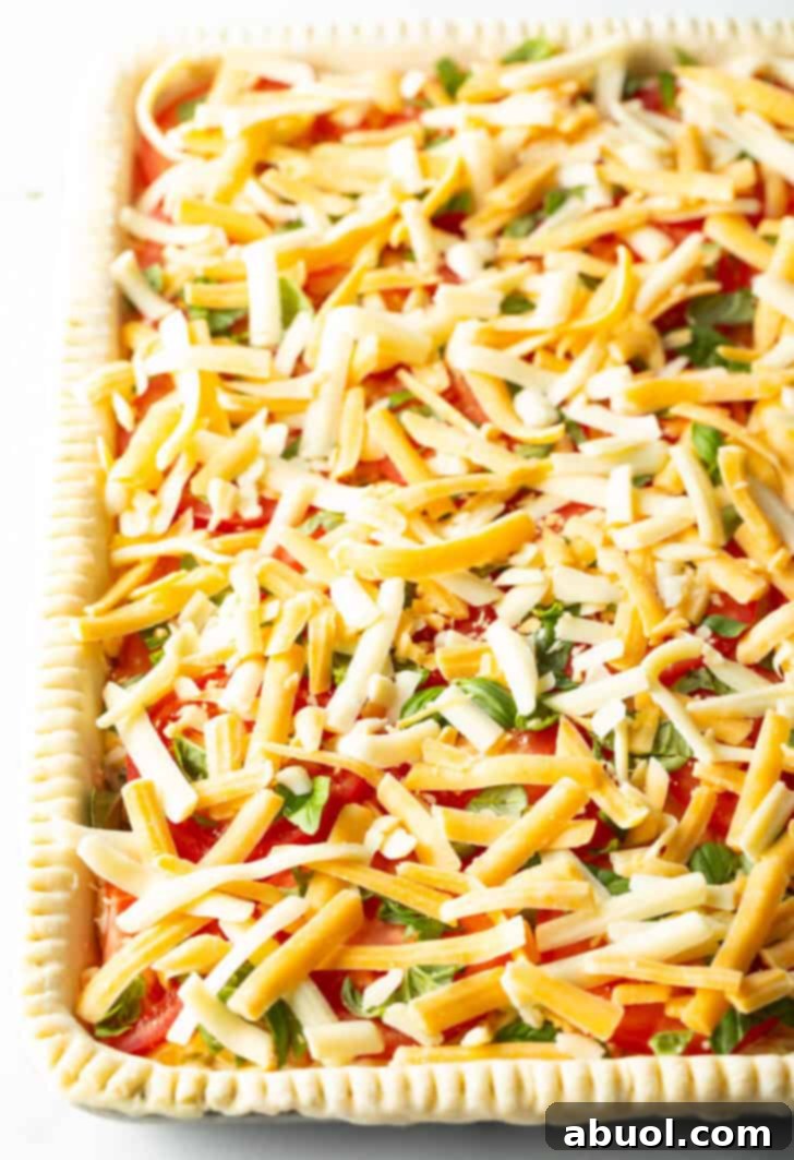 Fresh Garden Tomato Tart 11 Top down view of raw slices of tomato in an unbaked slab pie, topped with shredded cheese and sliced green onions.