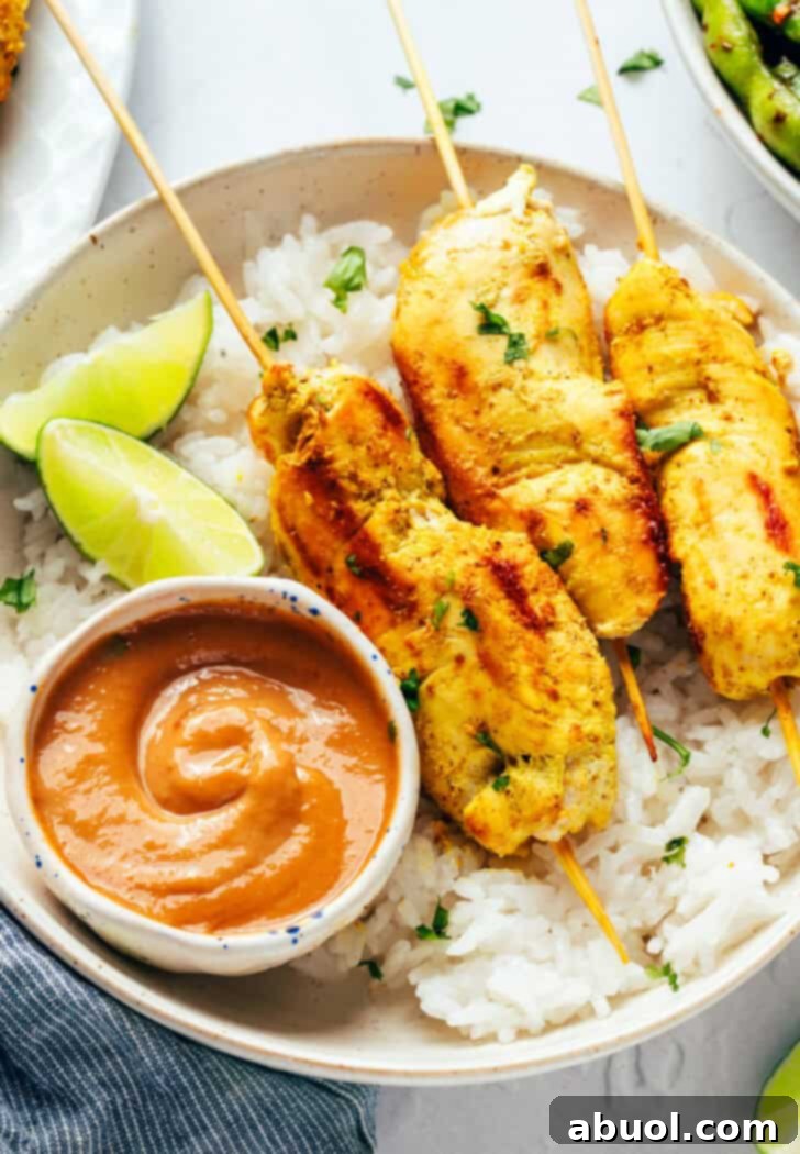 6 pieces of chicken satay on a white round plate with white rice, slices of lime and a white ramekin of peanut sauce.