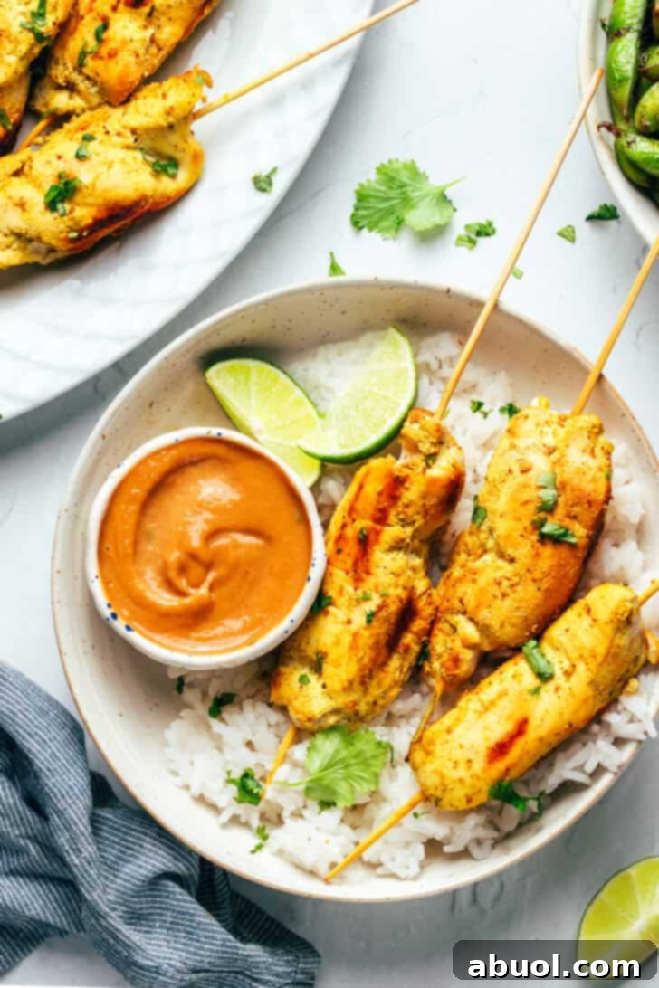 6 pieces of chicken satay on a white round plate with white rice, slices of lime and a white ramekin of peanut sauce.