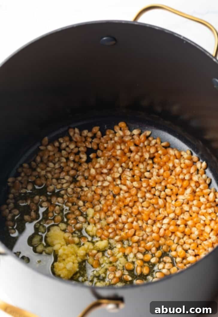 Raw popcorn kernels and ghee in a large black cooking pot.