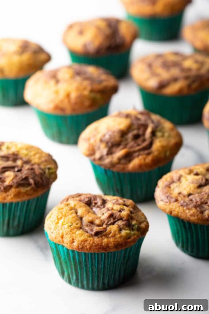 A dozen chocolate zucchini muffins with elegant Nutella swirls, presented in vibrant green cupcake wrappers, ready to be enjoyed.