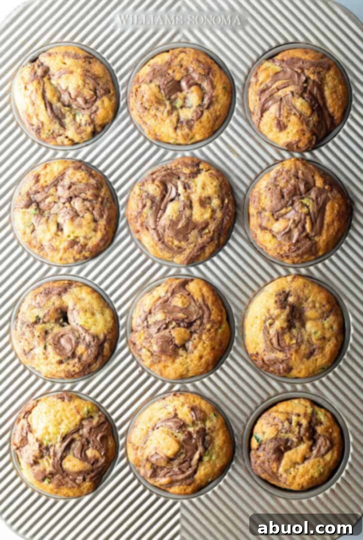 A top-down view showcasing a full dozen zucchini and Nutella muffins, still nestled perfectly in their baking tin, highlighting their delicious appearance.