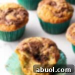 A dozen zucchini muffins with Nutella swirls, in green cupcake wrappers. One muffin has been split in half to show the inside.