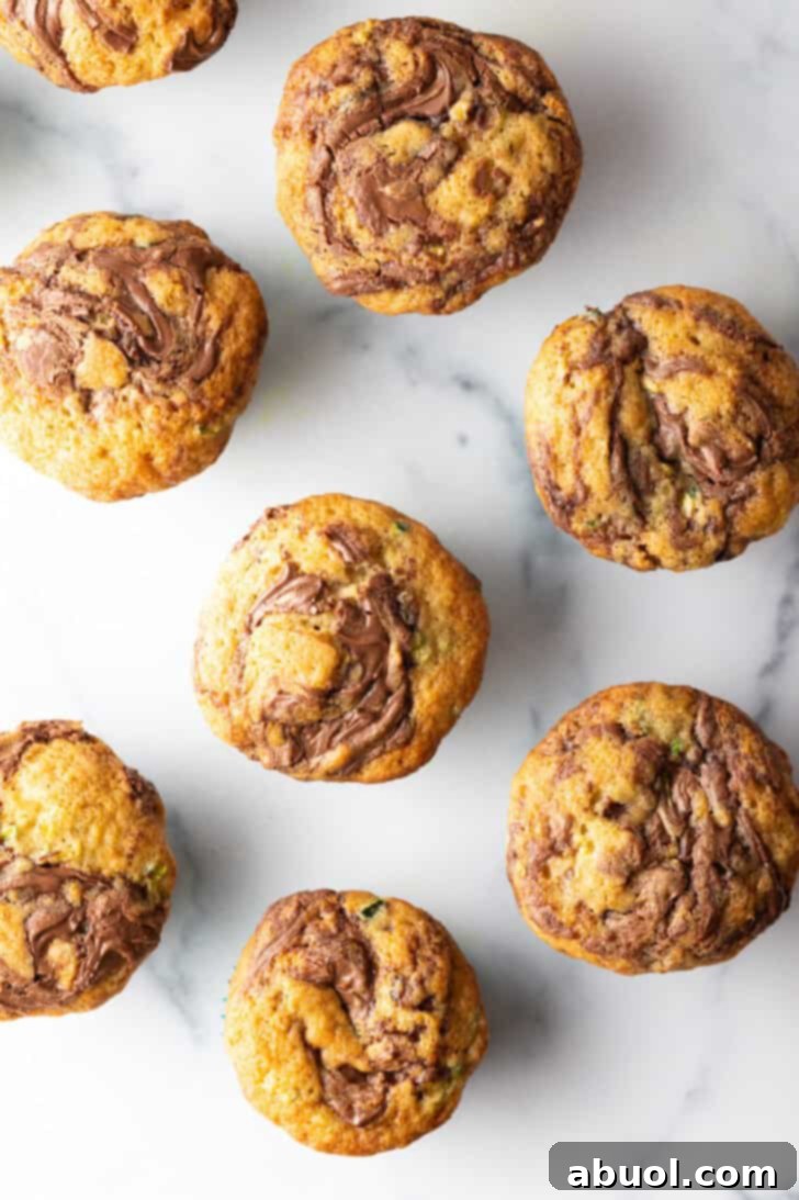 A top-down view of a dozen perfectly golden chocolate zucchini muffins, beautifully swirled with chocolate, nestled in a baking tin.
