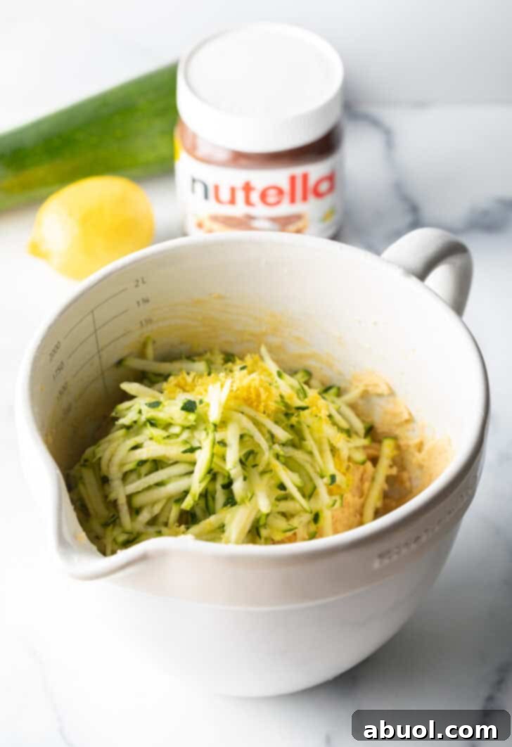 A white measuring bowl filled with fluffy shredded zucchini and delicate lemon zest, ready to be incorporated into the muffin batter.