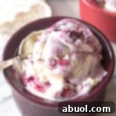Dark bowl with blueberry pie ice cream. A spoon is taking a scoop from the bowl.
