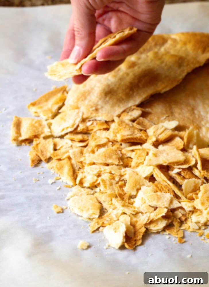 Hand cracking a piece of baked pie crust into small, irregular pieces.