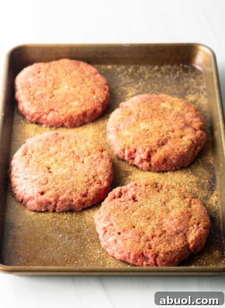 Air Fryer Burger Perfection 5 4 raw seasoned burger patties on a baking sheet.