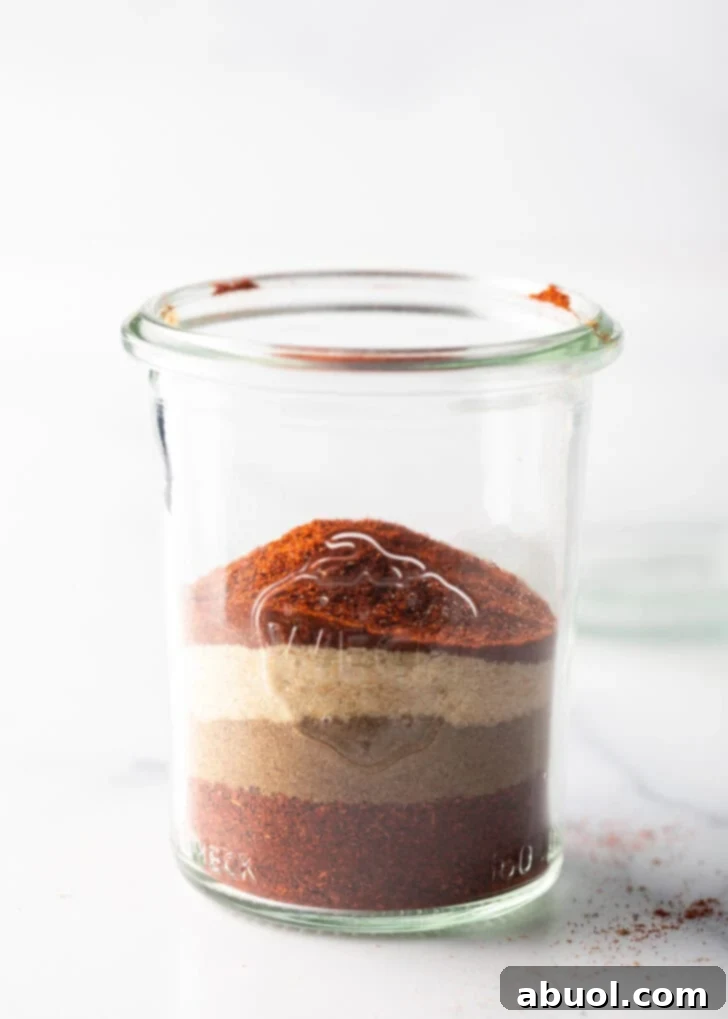 Layers of different seasonings distinctively visible in a tall glass jar, before mixing.