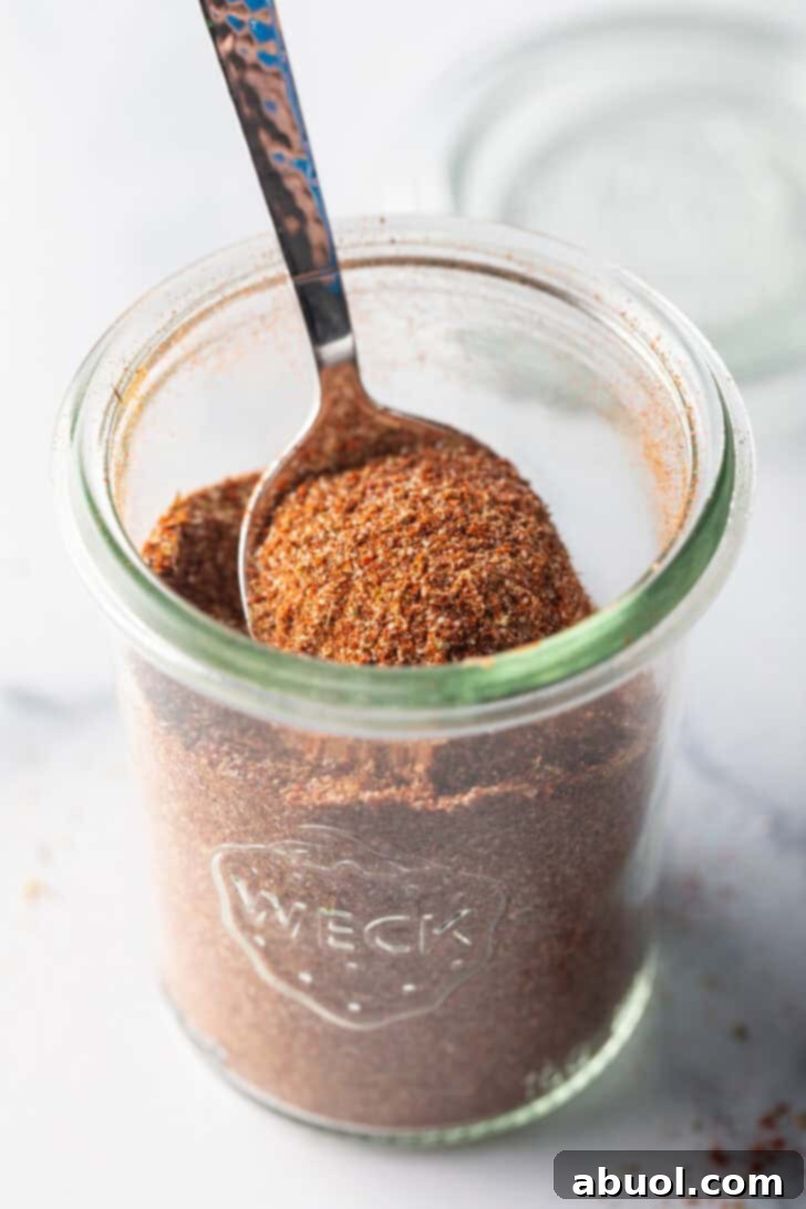 A spoon digging into a small glass jarful of homemade chicken taco seasoning, inviting use.