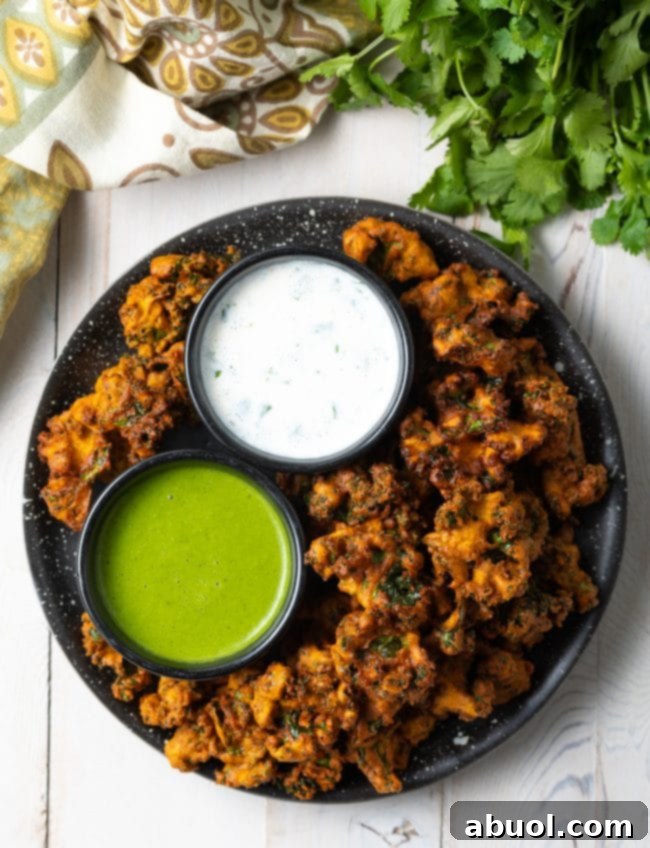 Crispy Kale and Vegetable Pakora 2 Top down view plate with kale vegetable pakora, with a ramekin of white sauce and ramekin of green sauce.