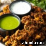 Plate with kale vegetable pakora, with a ramekin of white sauce and ramekin of green sauce.