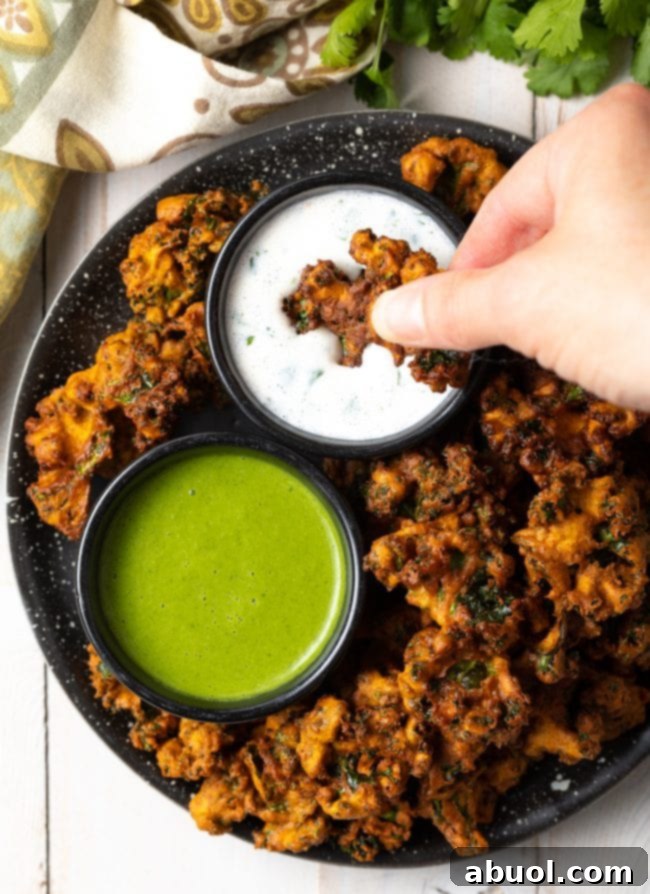 Crispy Kale and Vegetable Pakora 12 Top down view of a hand dipping a piece of crispy vegetable pakora into a ramekin of white sauce.