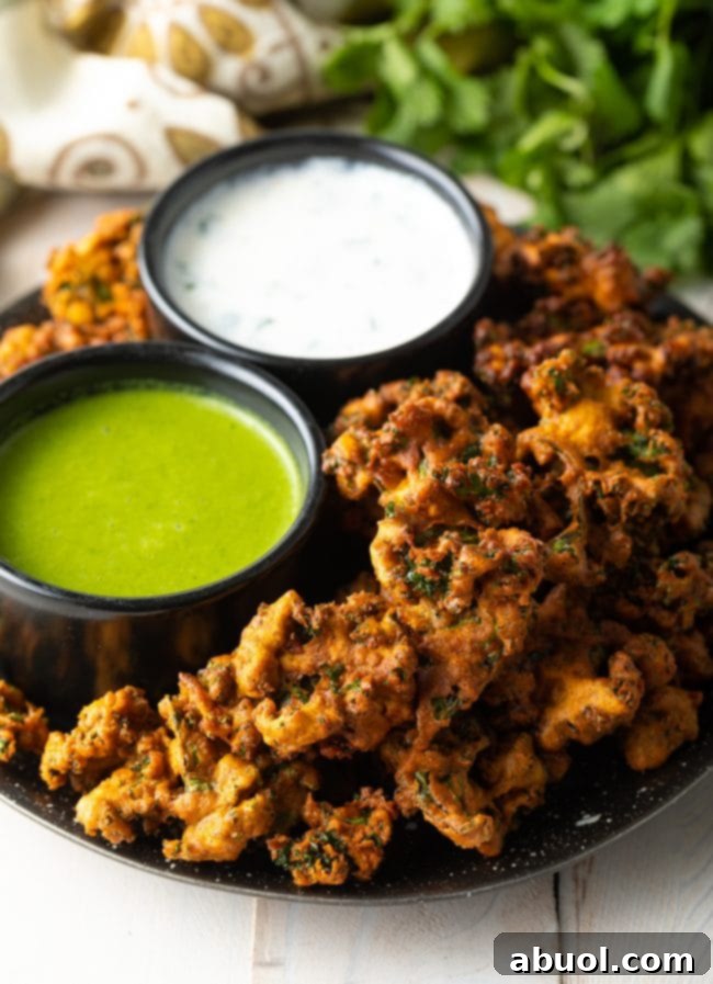 Crispy Kale and Vegetable Pakora 4 Plate with kale vegetable pakora, with a ramekin of white sauce and ramekin of green sauce.