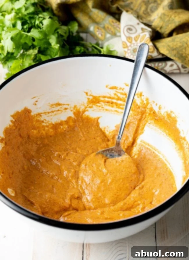 Crispy Kale and Vegetable Pakora 7 White mixing bowl with a light orange batter being mixed with a spoon.