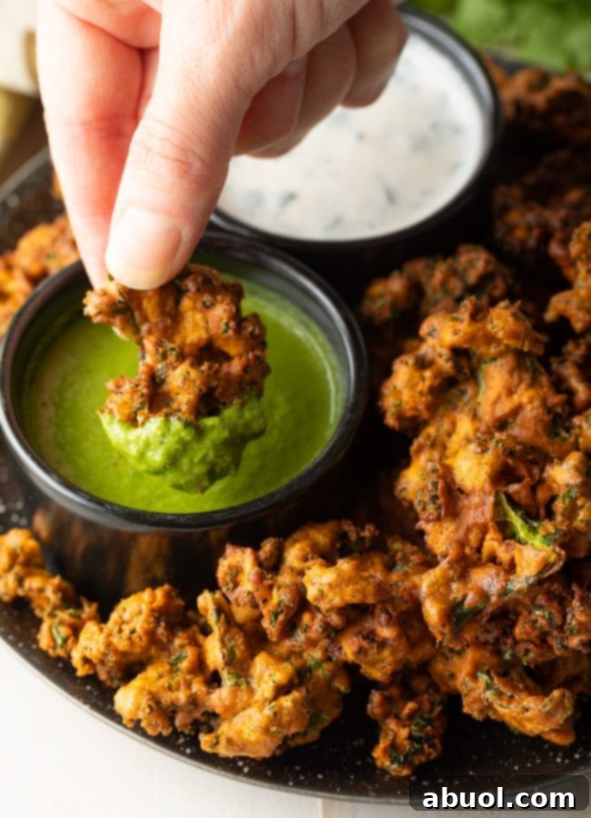 Crispy Kale and Vegetable Pakora 10 Hand dipping a piece of crispy vegetable pakora into a ramekin of green sauce.