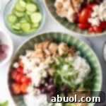 Greek chicken bowl with pieces of chicken, rice, sliced cherry tomatoes, kalamata olives, tzatziki sauce, cucumbers and feta cheese.