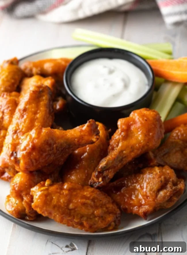 A plateful of golden, crispy baked buffalo chicken wings, served with a ramekin of ranch dressing, fresh carrot sticks, and crisp celery sticks, ready to be enjoyed.