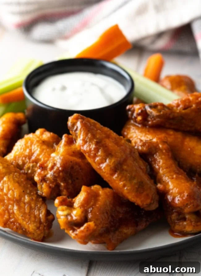 A beautifully presented platter of golden oven-baked buffalo chicken wings, with a side of creamy ranch dressing and fresh, crisp carrot and celery sticks.