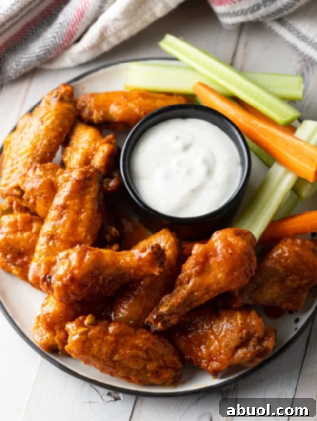 A vibrant platter of oven-baked buffalo chicken wings, glistening with sauce, served alongside a small black ramekin of creamy ranch dressing, and refreshing carrot and celery sticks.