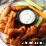 A plateful of golden, crispy baked buffalo chicken wings, served with a ramekin of ranch dressing, fresh carrot sticks, and crisp celery sticks, ready to be enjoyed.