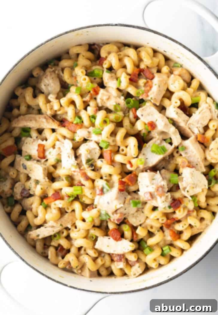 Top down view of creamy pasta with chicken, bacon, and vibrant green onions, ready to serve.