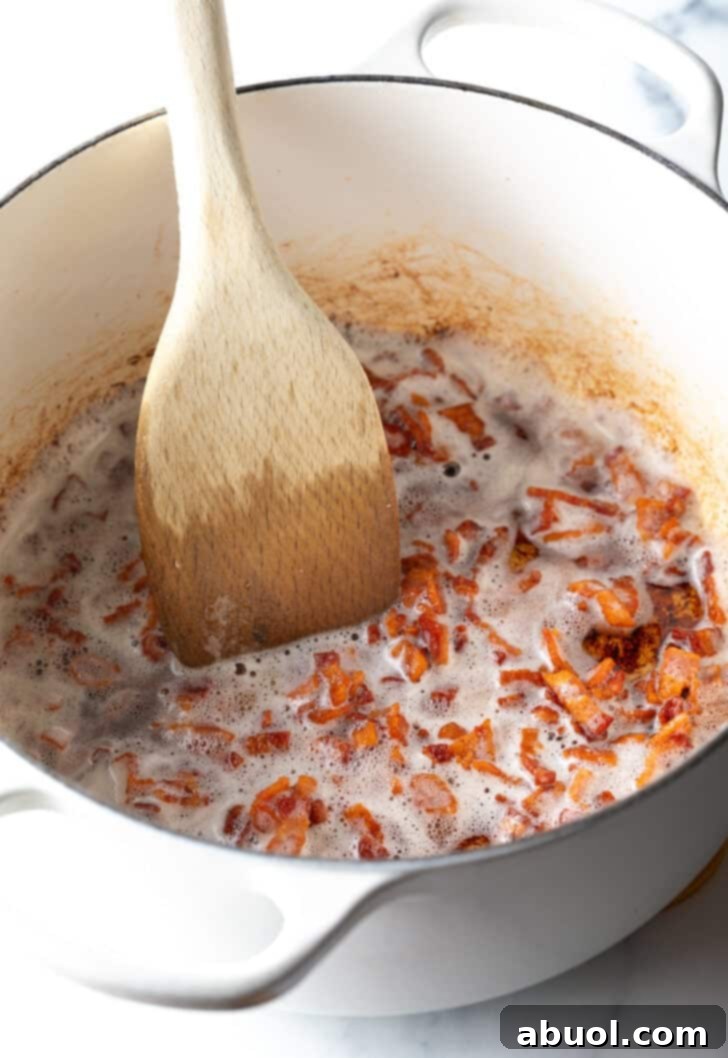 Chopped pieces of bacon sizzling in a white cooking pot, being stirred with a wooden spatula.