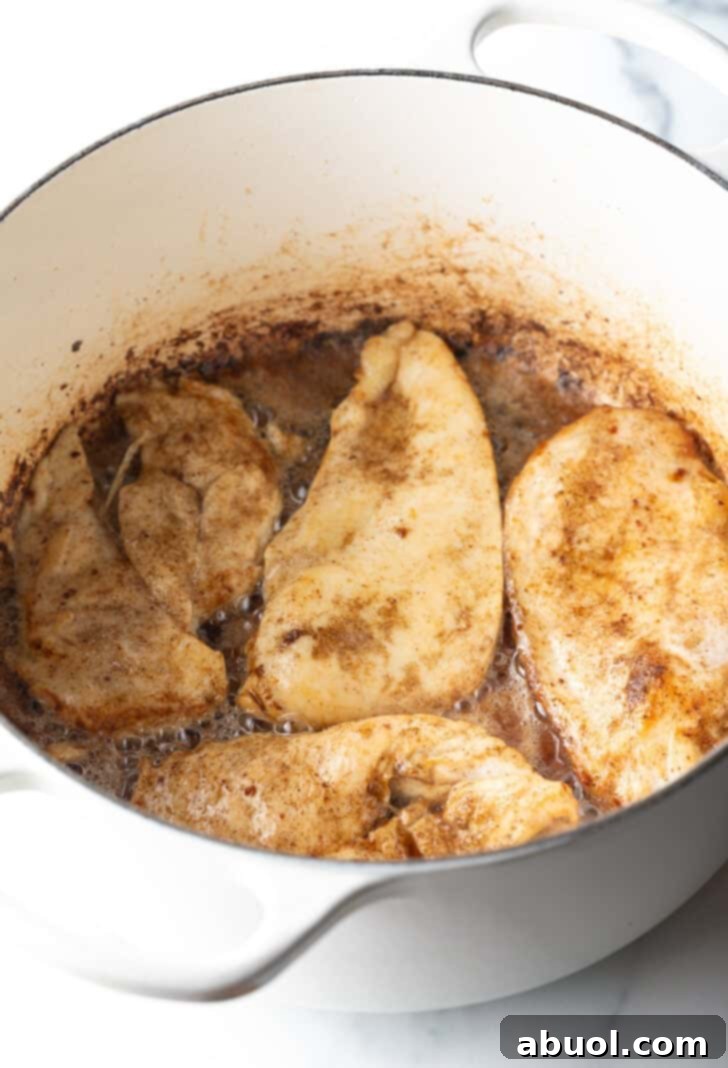 Four chicken breasts browning evenly in a deep white pot.