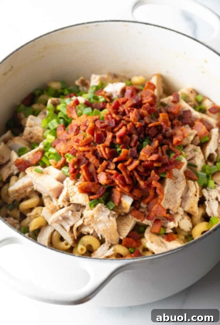 Adding chopped cooked bacon on top of the pasta and chicken in a cooking pot.