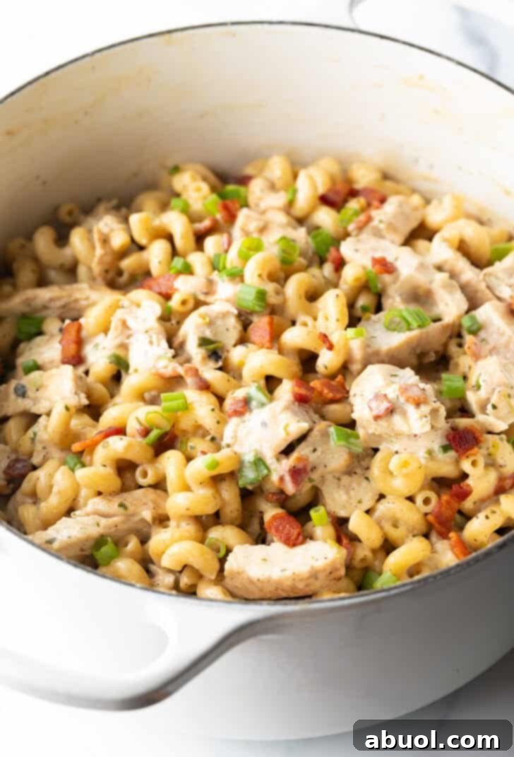 A white pot cooking pasta with chicken and bacon, simmering in a rich sauce.