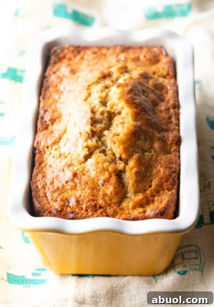 A perfectly baked, golden-brown 4-ingredient banana bread loaf resting in a white and yellow loaf pan, just out of the oven.