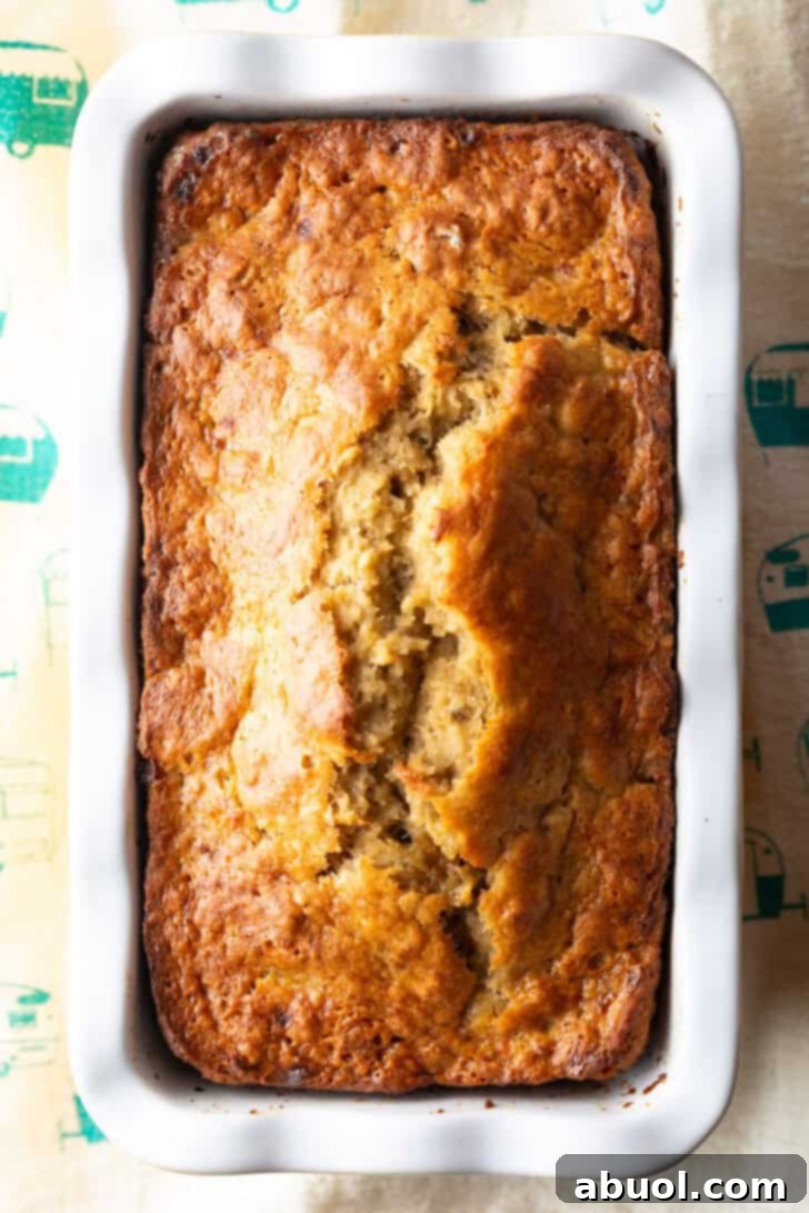 A top-down view of a perfectly baked 4-ingredient banana bread loaf, still warm in its white and yellow loaf pan, ready to be sliced and enjoyed.
