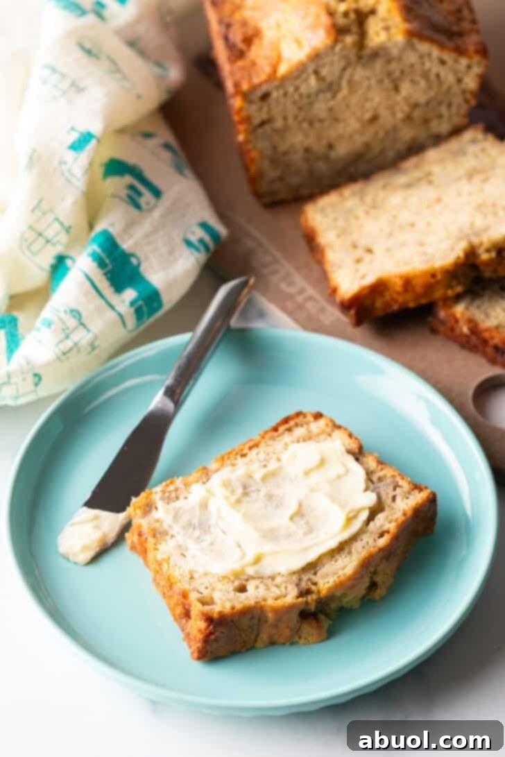 A delicious slice of 4-ingredient banana bread, generously slathered with butter, presented on a vibrant blue plate with a knife.