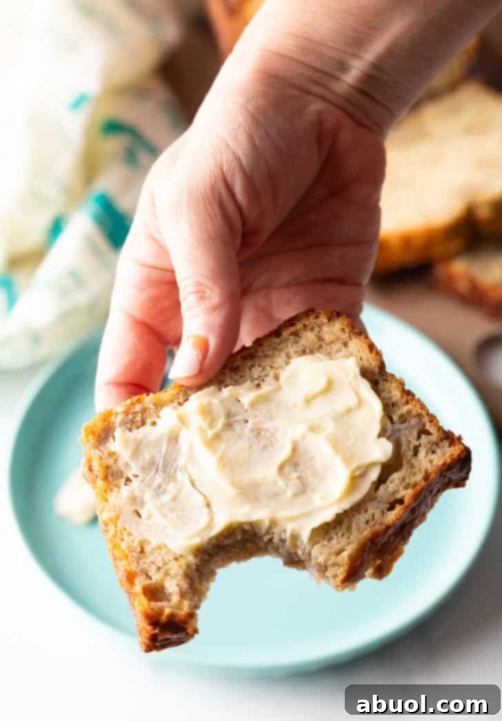 A hand holds a tempting slice of banana bread, buttery and soft, with a bite playfully taken from the corner.