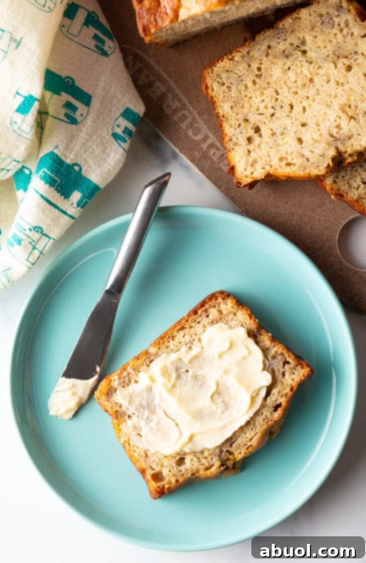 A delectable slice of 4-ingredient banana bread, generously slathered with soft butter, rests on a charming blue plate alongside a knife.