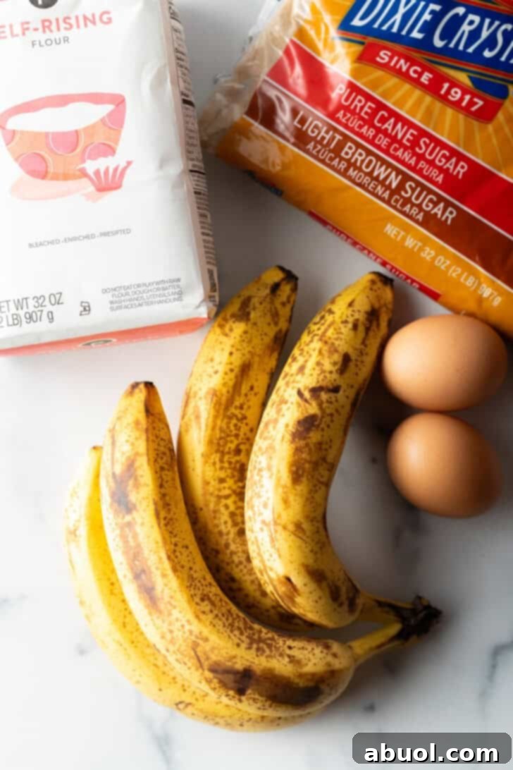 A top-down view of all the simple ingredients laid out for 4-ingredient banana bread: a bunch of ripe bananas, a bag of self-rising flour, a bowl of brown sugar, and two eggs.