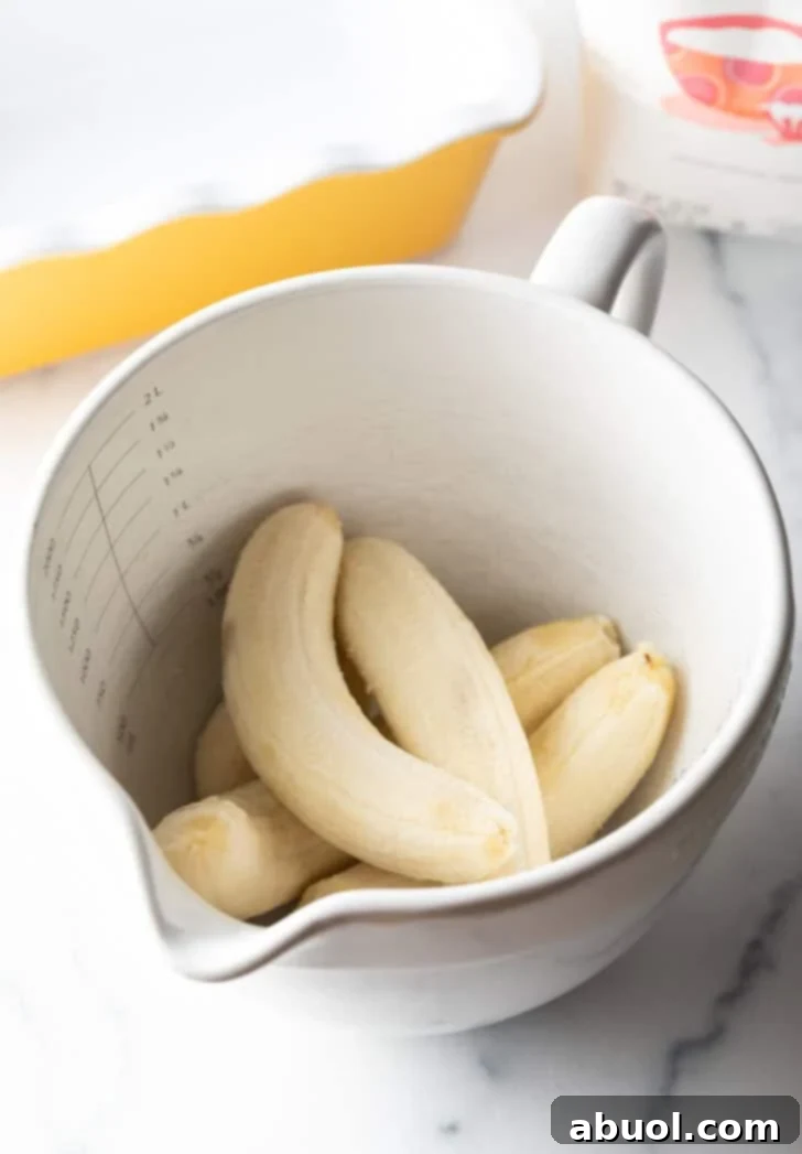 Five peeled ripe bananas in a large white mixing bowl, ready for mashing.