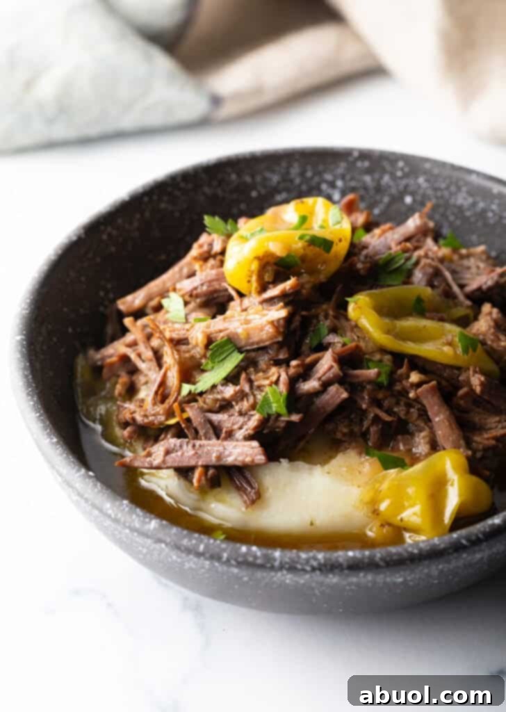 A black bowl filled with a comforting layer of mashed potatoes, generously topped with shredded Mississippi Pot Roast and bright red pepperoncinis, ready to be enjoyed.