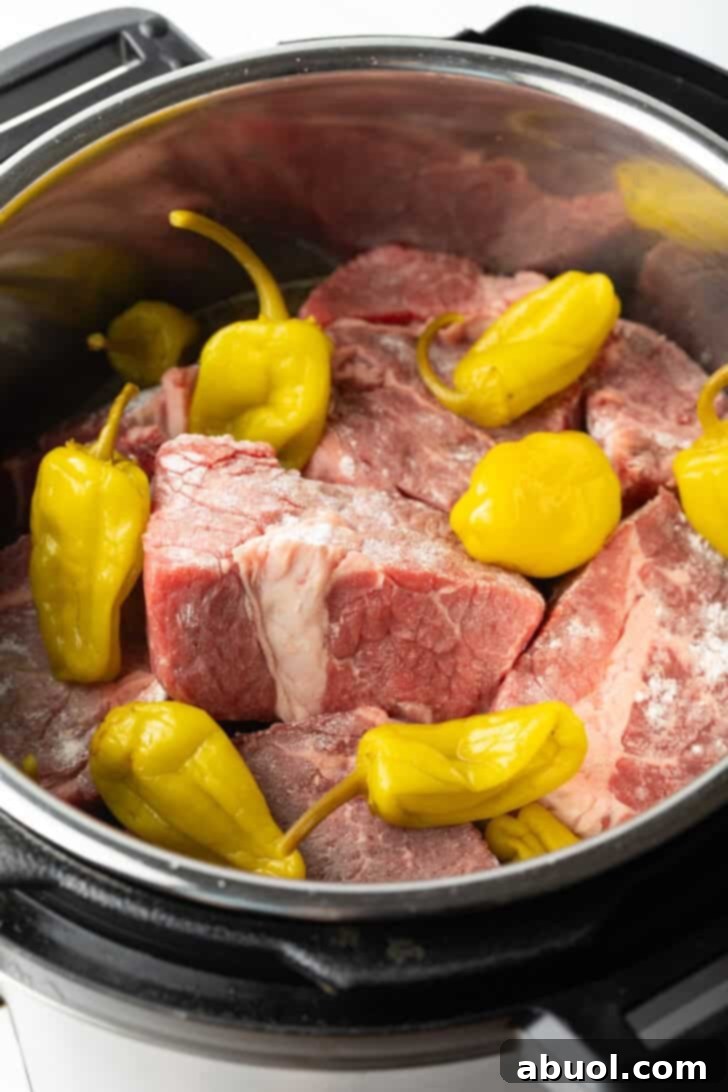 Generous chunks of floured raw beef nestled within the Instant Pot, topped with vibrant pepperoncini peppers, ready for pressure cooking.