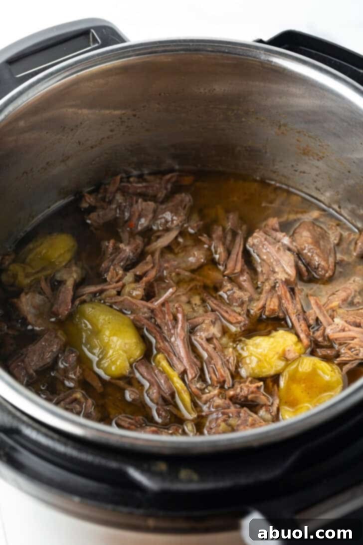 Close-up of tender, shredded pot roast resting in its rich juices within the Instant Pot, glistening and ready to be served.