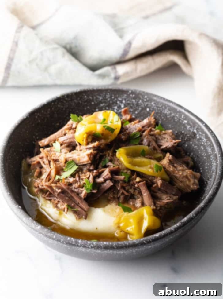 A black bowl featuring a comforting base of creamy mashed potatoes, generously adorned with tender, shredded Mississippi Pot Roast and bright pepperoncini garnishes, ready for enjoyment.