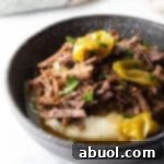 Black bowl with a layer of mashed potatoes topped with shredded pot roast and pepperoncinis.