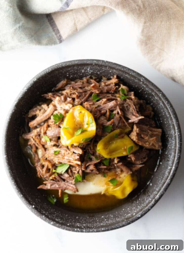 A top-down view of a black bowl, elegantly presenting a comforting mound of creamy mashed potatoes, generously crowned with tender, shredded Mississippi Pot Roast and garnished with vibrant pepperoncinis.
