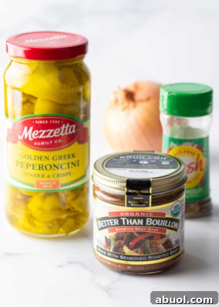 Recipe ingredients neatly arranged: A jar of rich beef bouillon, a jar of tangy pickled pepperoncinis, a container of fragrant Italian seasoning, and a whole, fresh onion.