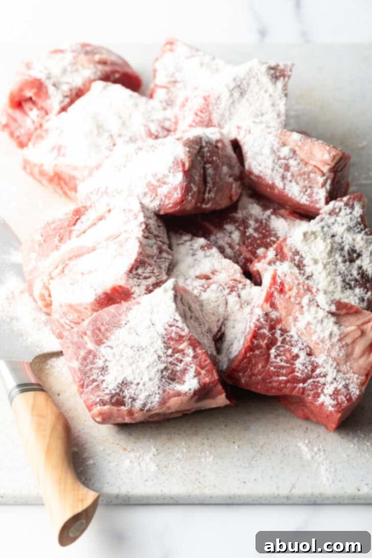 Generous chunks of raw beef, evenly coated in a dusting of all-purpose flour, ready for the next step in the recipe.