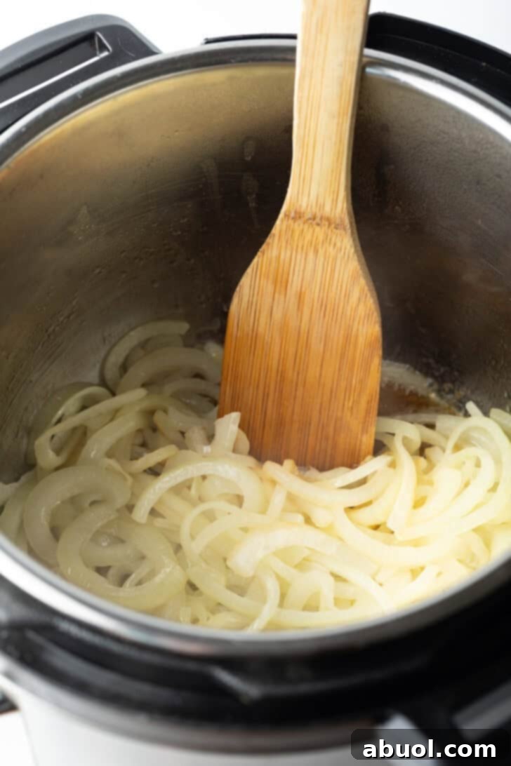 A wooden spatula gently sautéeing thin slices of onion in the inner pot of an Instant Pot, releasing their fragrant aroma.