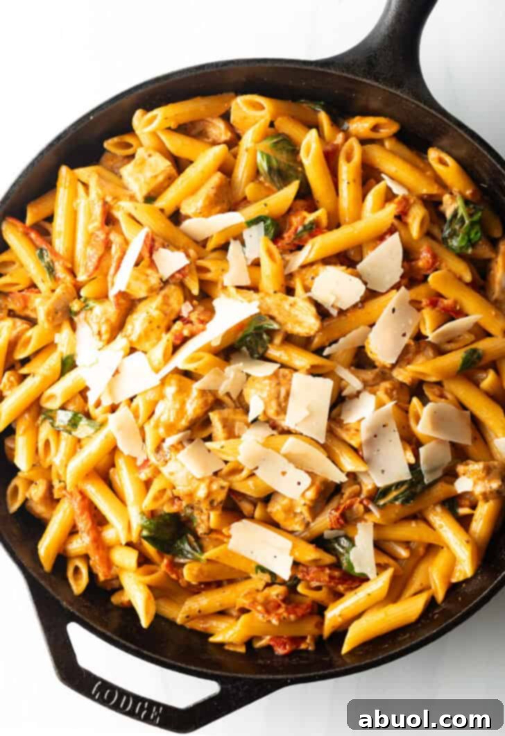 A cast iron skillet brimming with creamy Marry Me Chicken Pasta, featuring golden chicken pieces, penne noodles, and vibrant sun-dried tomatoes.