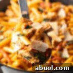 A large spoonful of creamy Marry Me Chicken Pasta, featuring tender chicken, penne, and sun-dried tomatoes, held up enticingly.