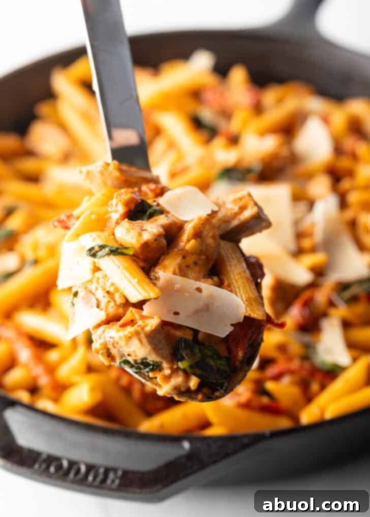 A generous spoonful of creamy Marry Me Chicken Pasta, showcasing tender chicken, penne, and sun-dried tomatoes, lifted from the skillet.